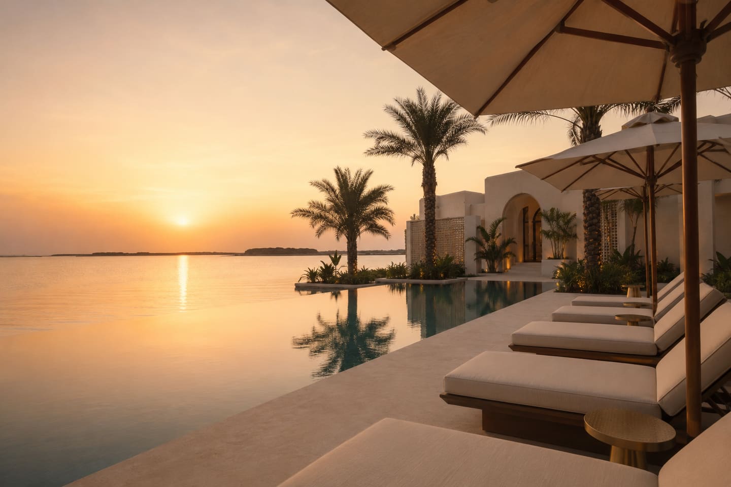 Transats et parasols au bord de la piscine à débordement, vue sur l’océan au coucher du soleil.